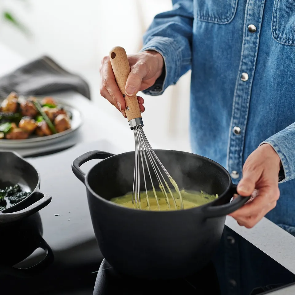 Whisking sauce in pan. Person grips wooden handle, blending ingredients smoothly.