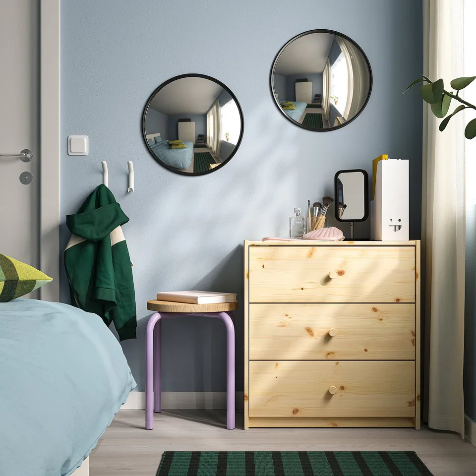 Bedroom corner with dresser, stool, and two black convex mirrors reflecting room. Green towel nearby.