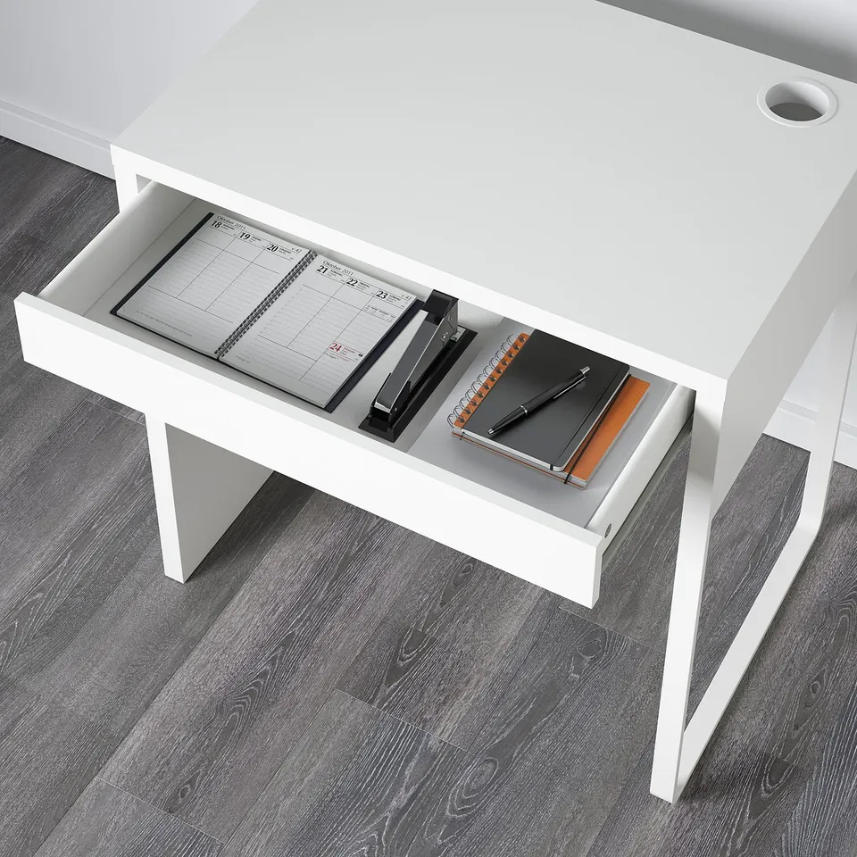Open white desk drawer revealing notebook, pen holder, and stationery.