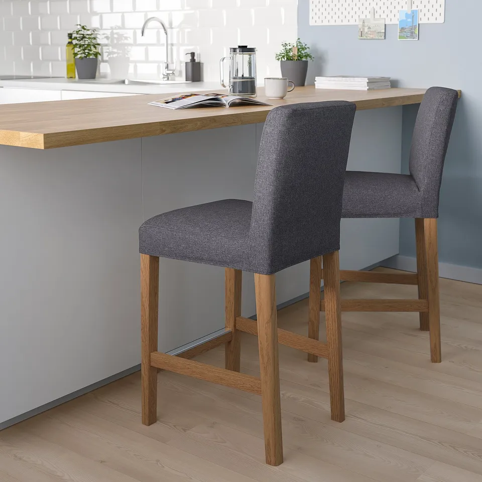 Grey barstool with wood legs, cushion, counter, coffee, dishes, plants.