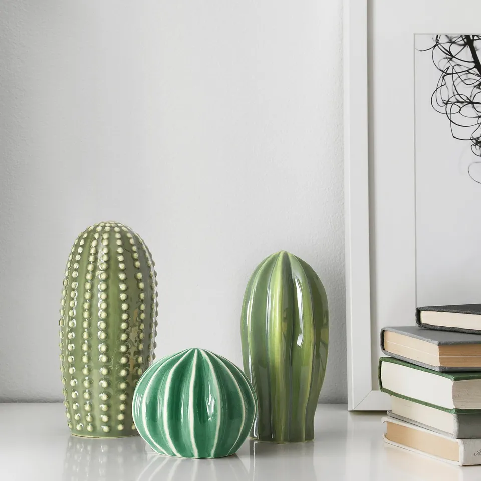 Three ceramic cacti in shades of green displayed on a white surface, resembling real plants without care needs.