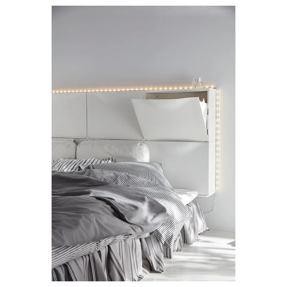 White TRONES cabinet atop bed, striped linens, soft lighting.