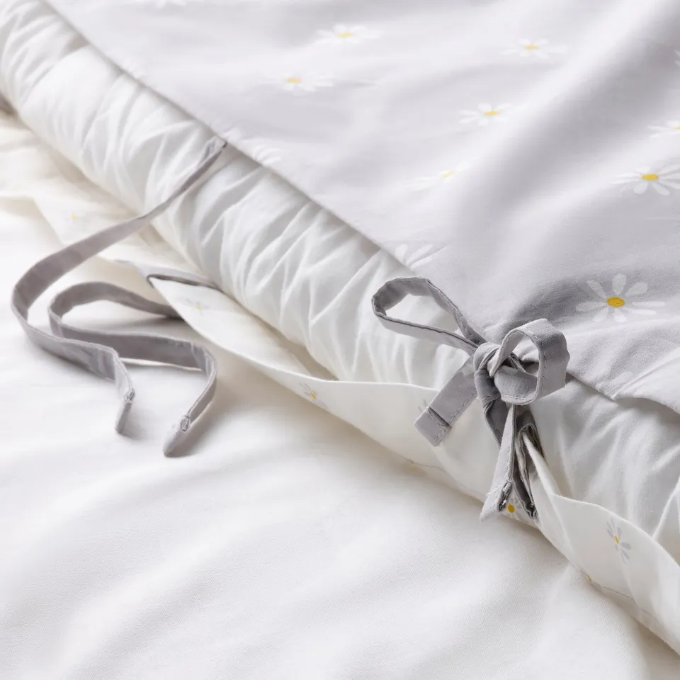 Rolled white duvet with yellow daisies, grey ribbon closure. Moisture-absorbing, breathable cotton percale, ideal for cool sleep.