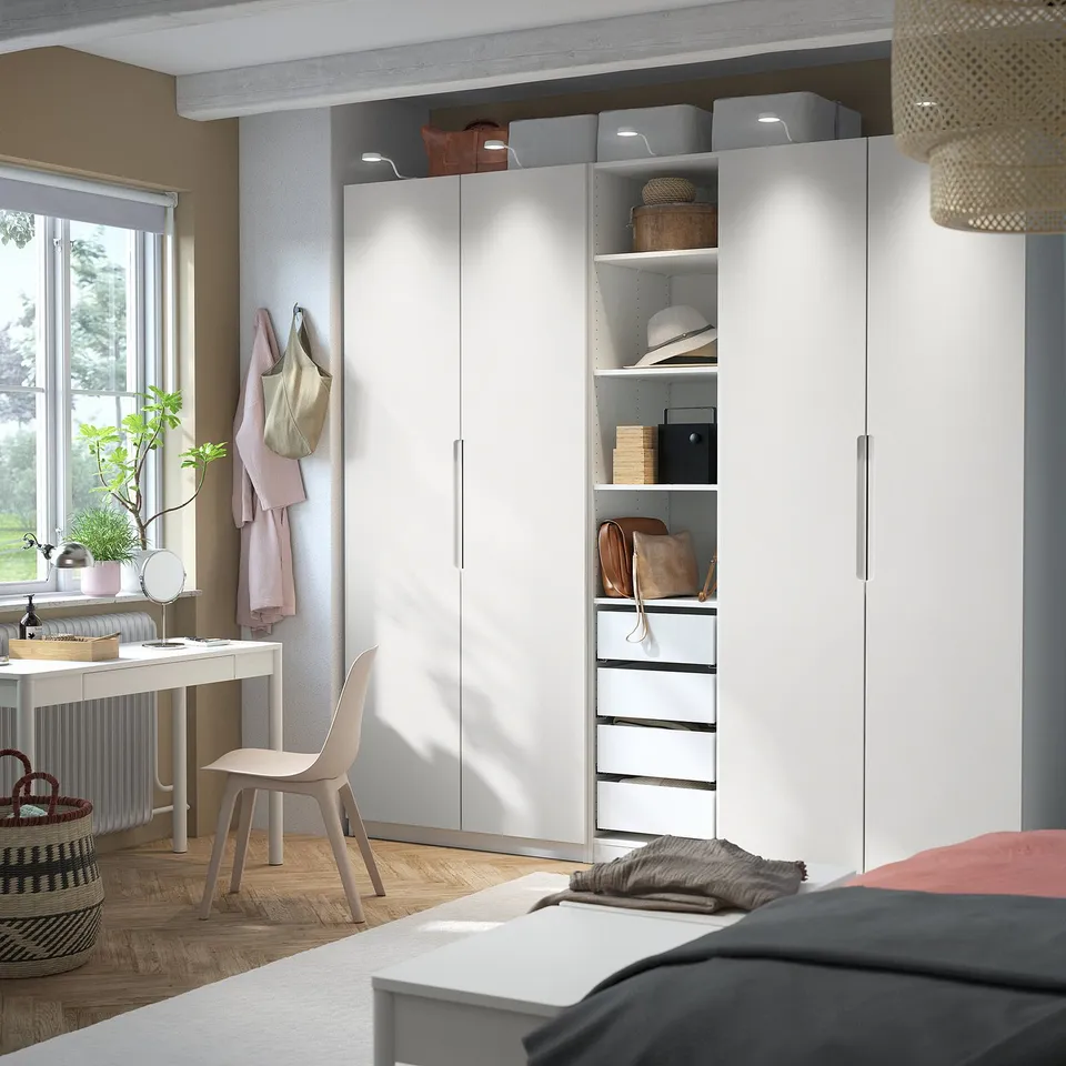 Modern bedroom with PAX wardrobe, desk, and plant.