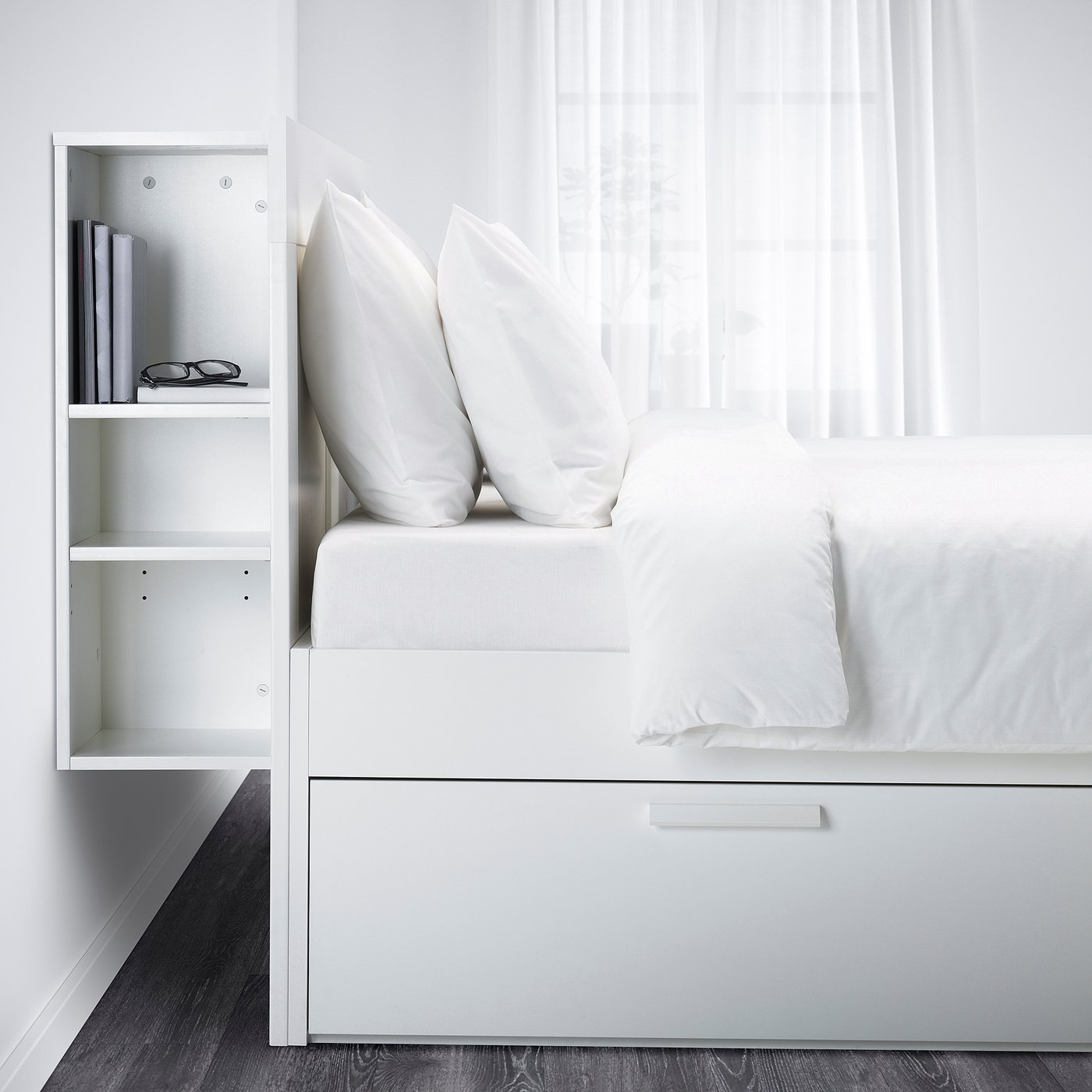White BRIMNES bed with storage, headboard shelves, fluffy pillows, white comforter, hidden drawers, sheer curtains.