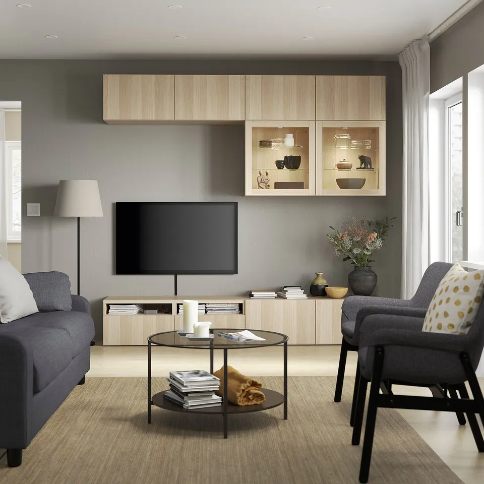 Modern living room: grey walls, SINDVIK tv unit, glass cases, blue couch, grey armchair with yellow pillow, circular coffee table on light wood floor.