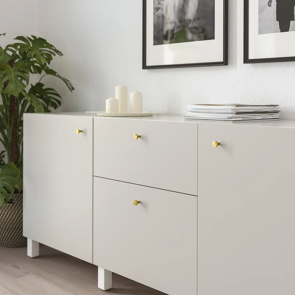 White sideboard with gold knobs displaying candles and magazines, framed wall art visible.