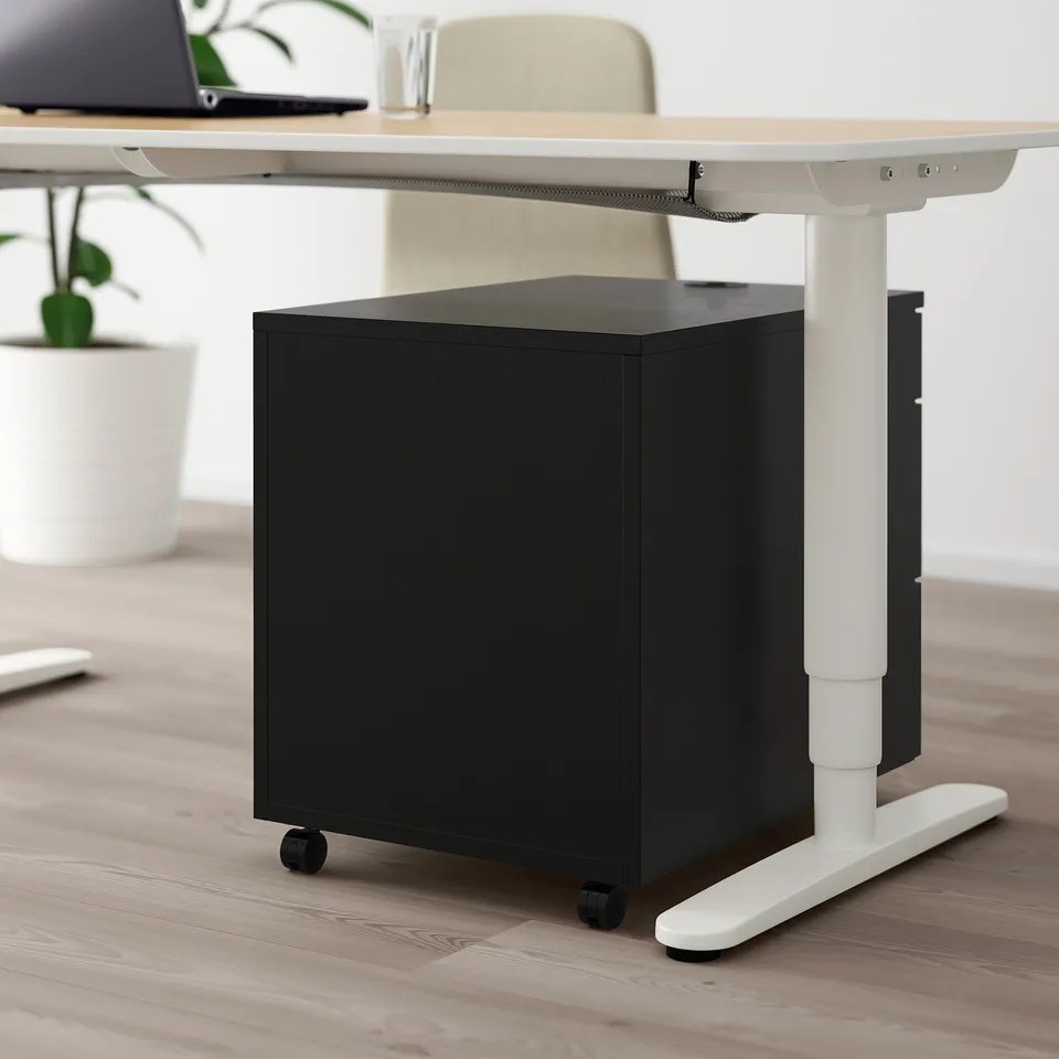 Black rolling storage cabinet under adjustable white desk, featuring secure combination lock and gentle-closing drawers.