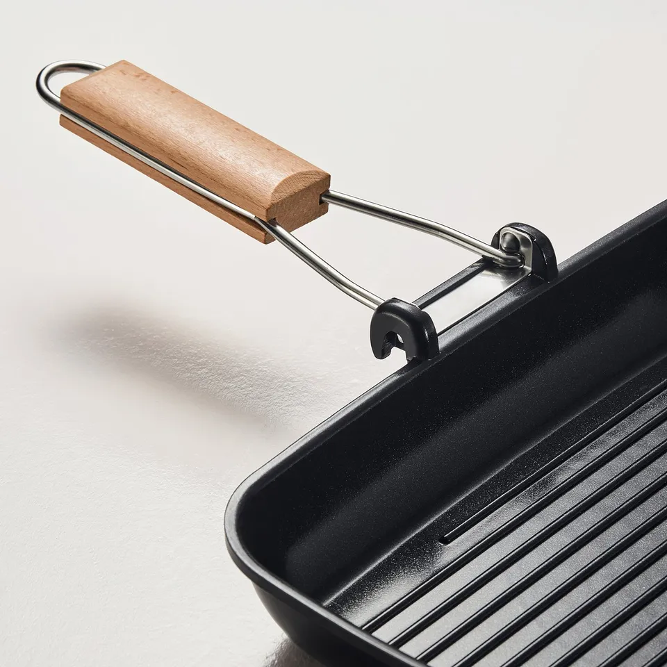 Close-up of a high-quality grill pan. A sturdy wooden handle with a folded design and a ribbed cooking surface.