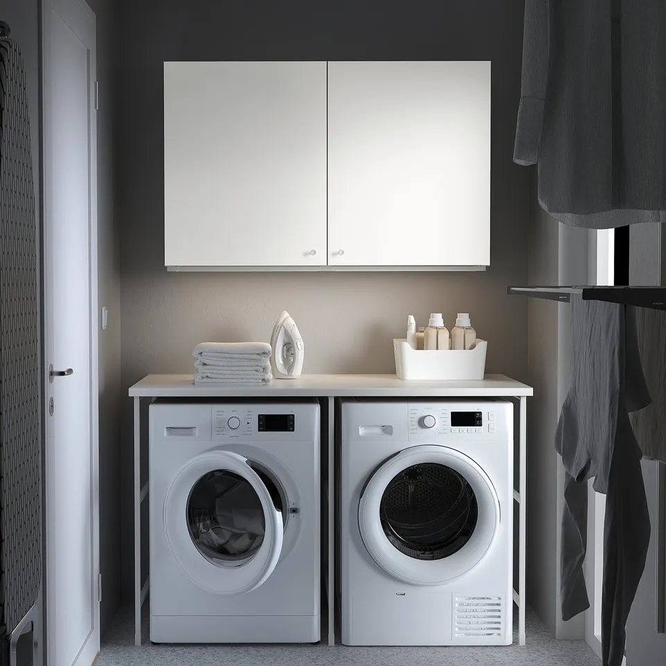 Modern laundry room with white ENHET wall cabinet, washing machine, and dryer. Cabinet offers closed storage above machines.