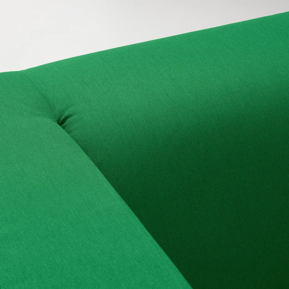 Bright green sofa fabric close-up. Texture smooth, densely woven, uniform colour. Cushion shows slight indentation from use.