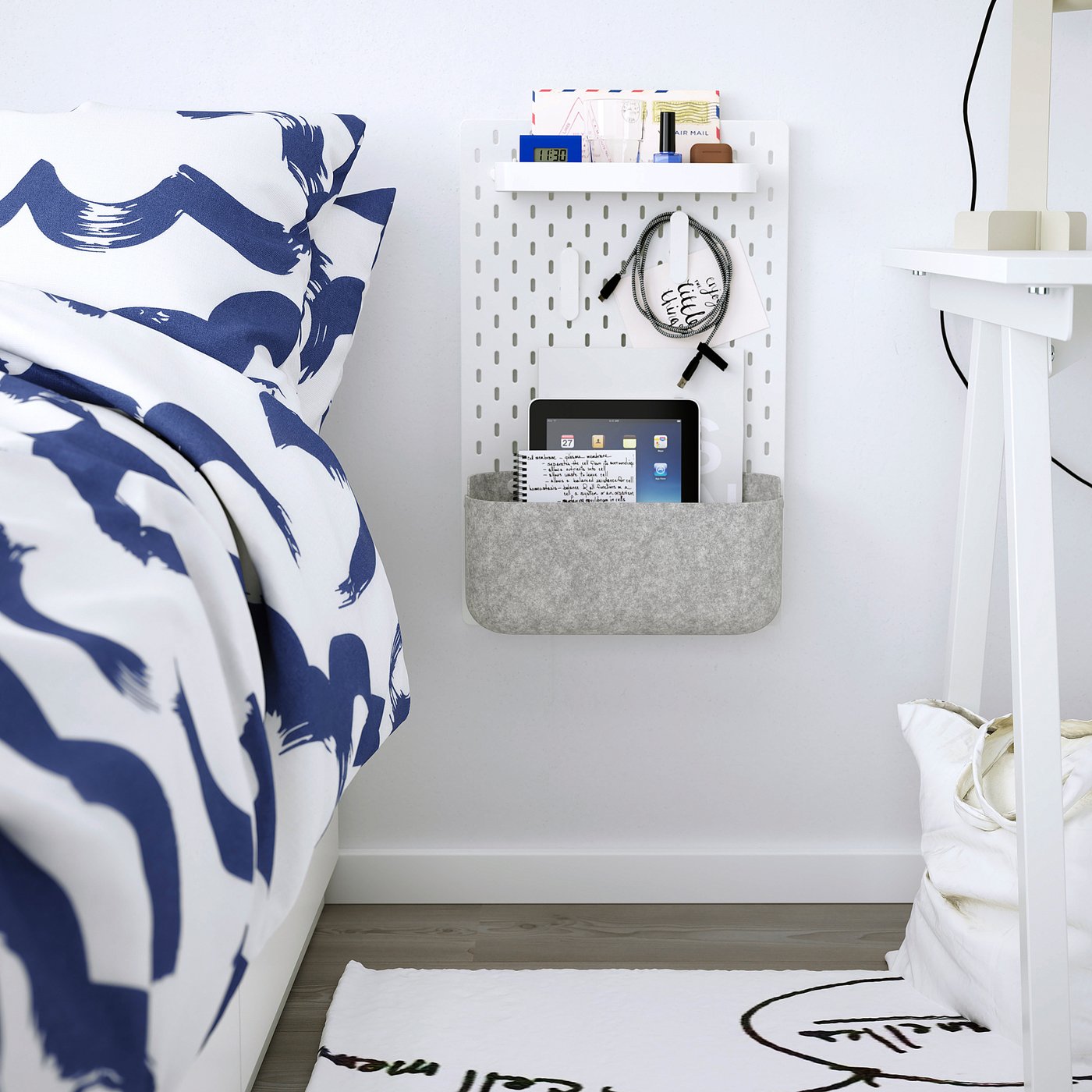 Bedroom with blue/white pillow & comforter. Pegboard with tablet basket.