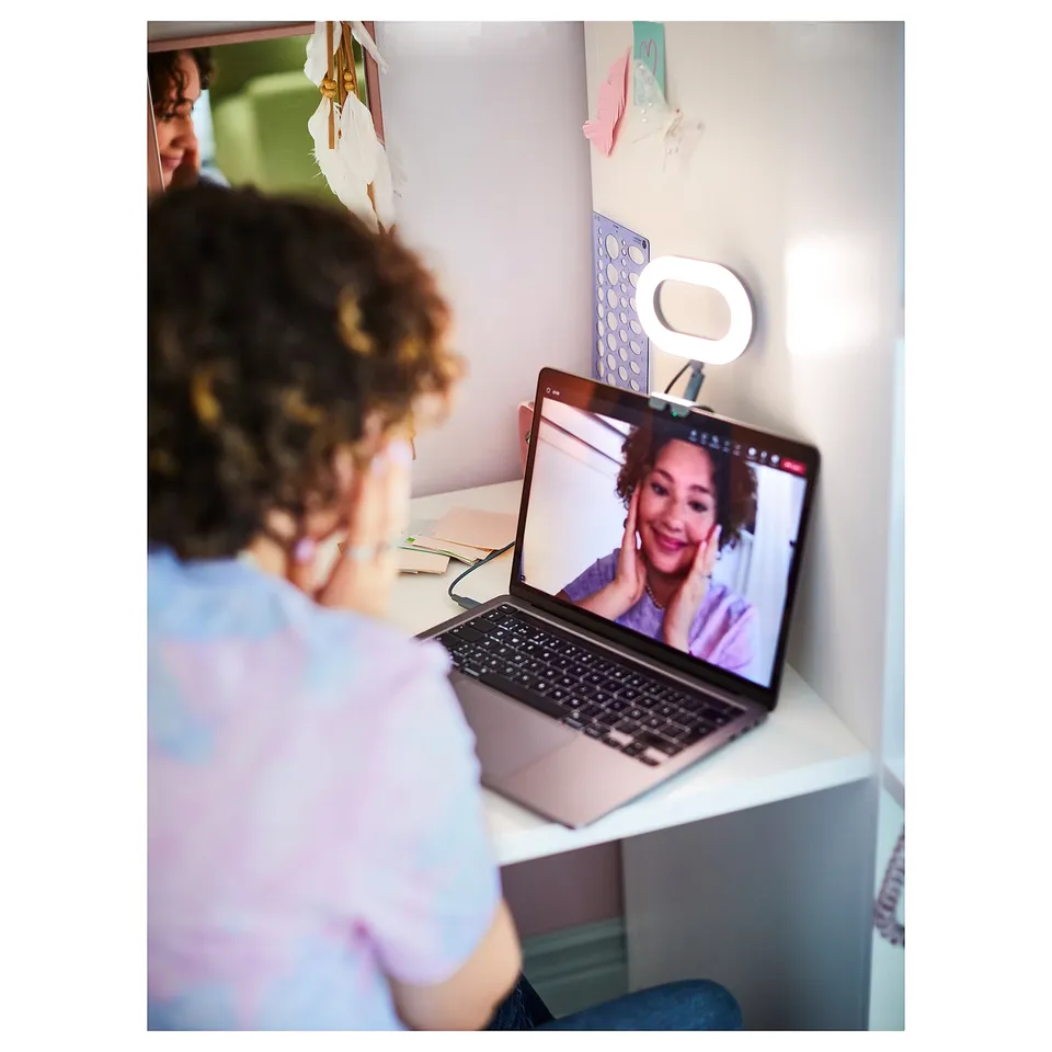 Person with curly hair on video call, smiling at laptop with ring light attached.