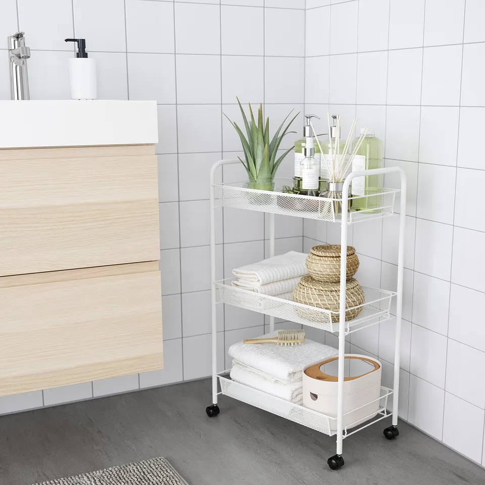 Bathroom storage trolley HORNAVAN, white, metal & plastic, three-tiered. Fits neatly beside wooden vanity, holds towels, plants, & toiletries.