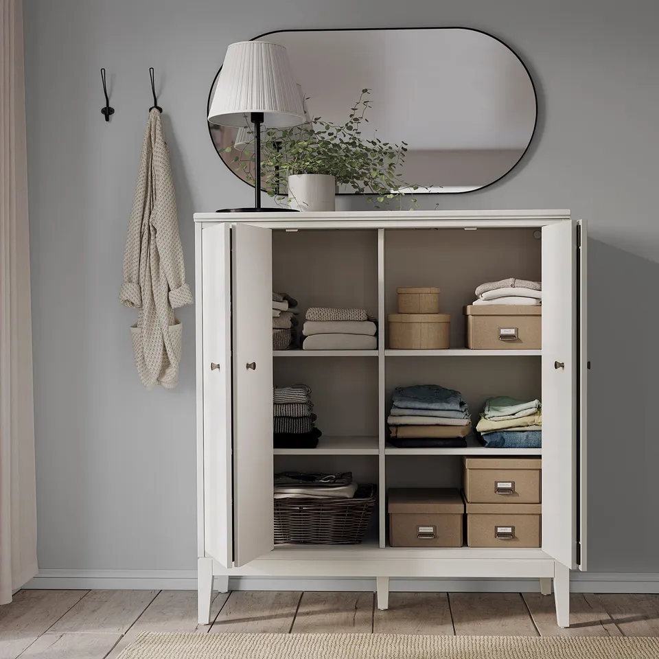 White IDANÄS cabinet open, clothes & boxes on shelves, mirror, lamp.