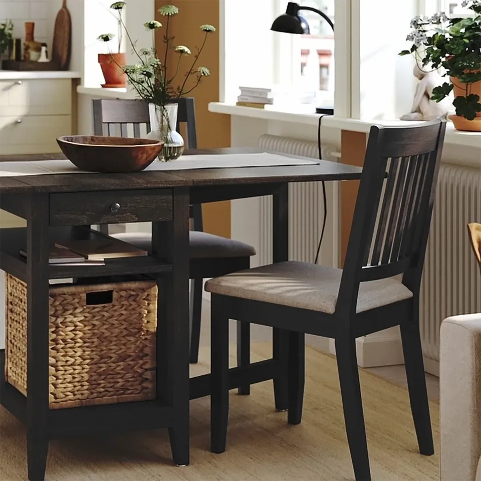 Wooden chair with woven seat and basket storage, positioned near a rustic table with a bowl and flower vase.
