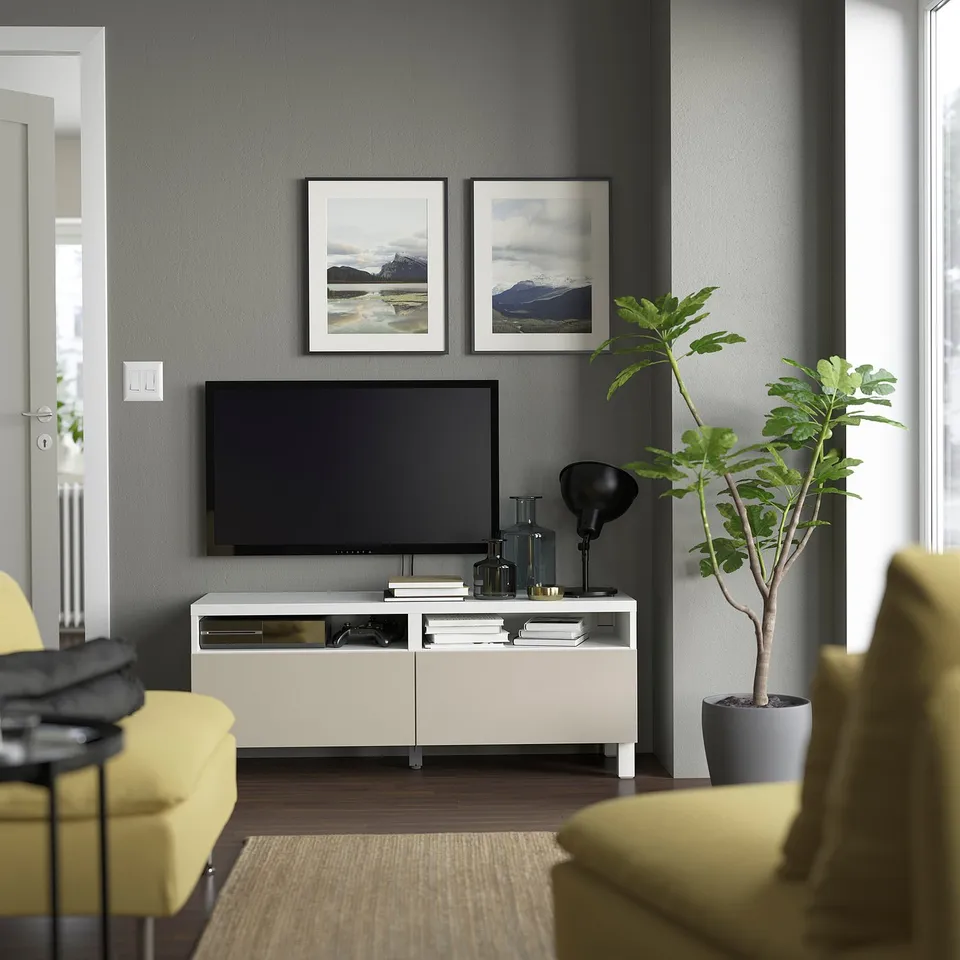 Modern living room with BESTÅ white tv stand, flat-screen tv, framed photos, yellow couch, and green plant against grey wall.