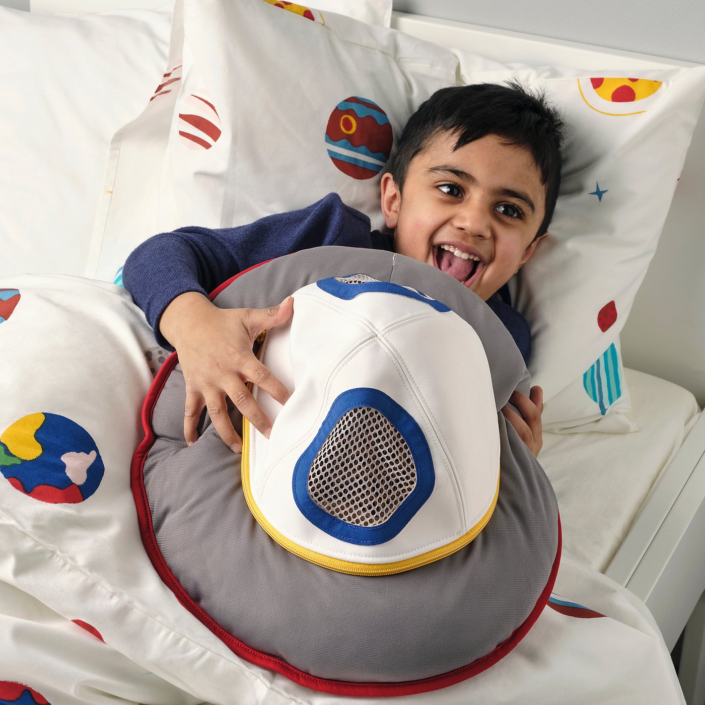 Child plays with AFTONSPARV spaceship pillow in hospital, smiling.