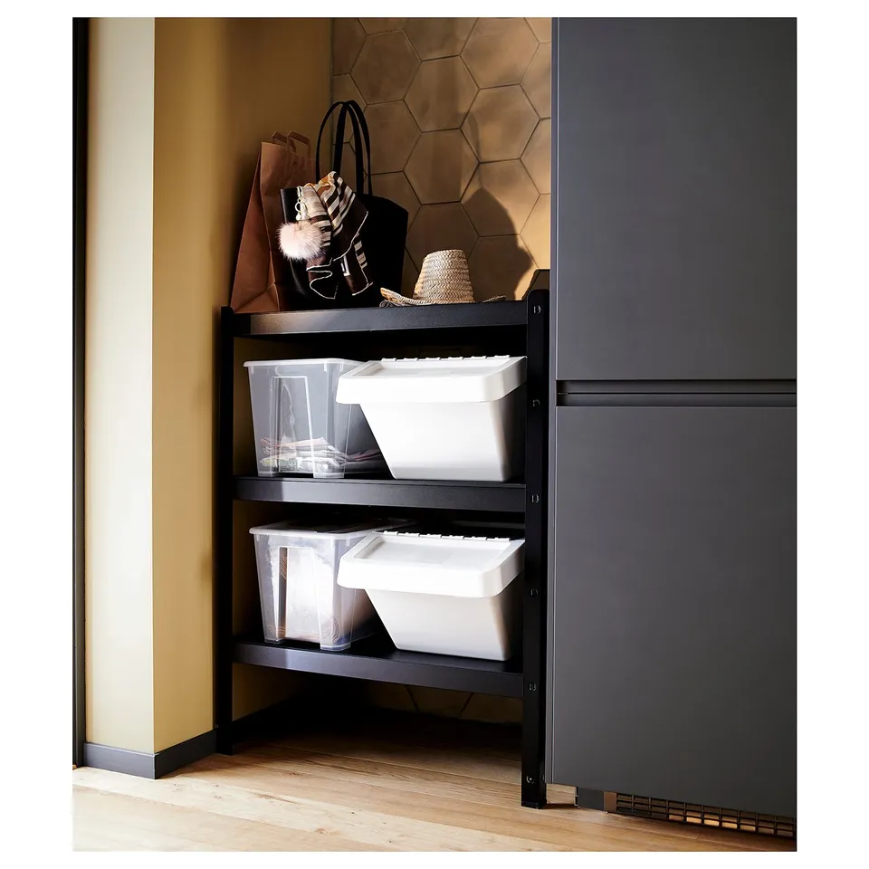 Black metal storage rack with two large white containers, positioned in a corner against a grey cabinet.