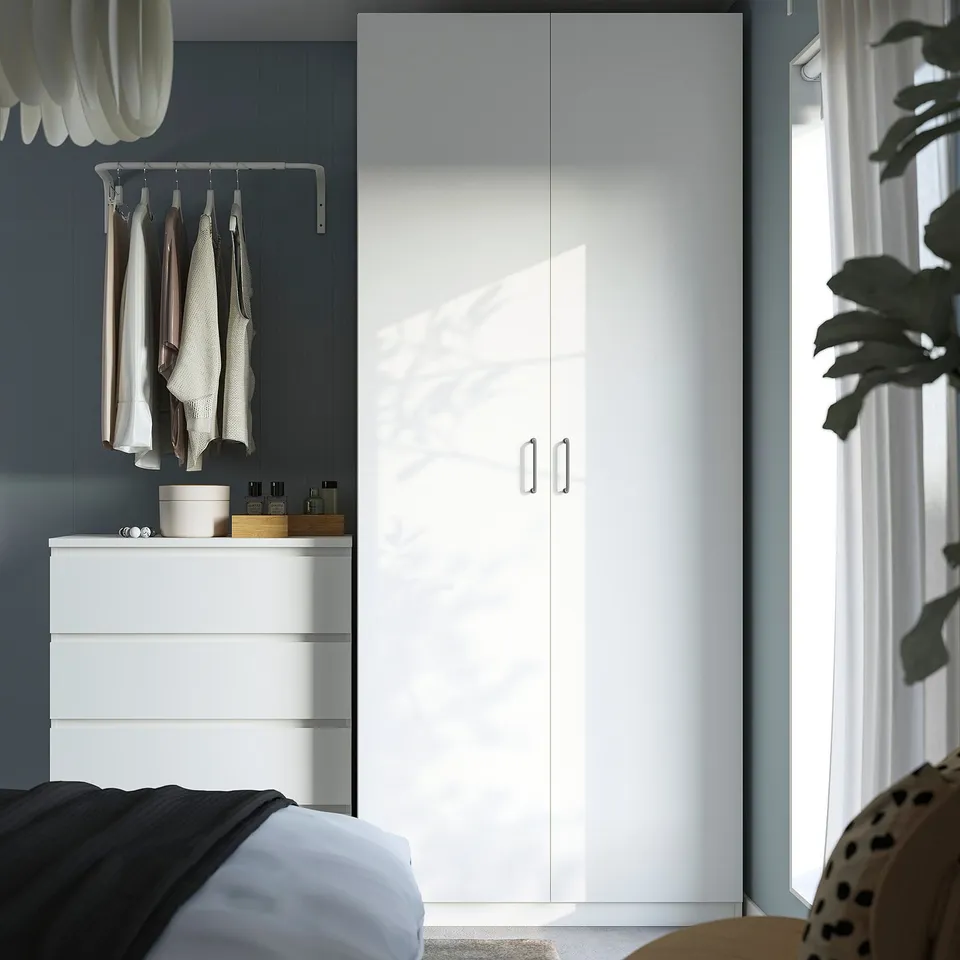 Minimalist bedroom with large white PAX wardrobe. Tall, sleek design featuring doors, hanging rail, and shelves.