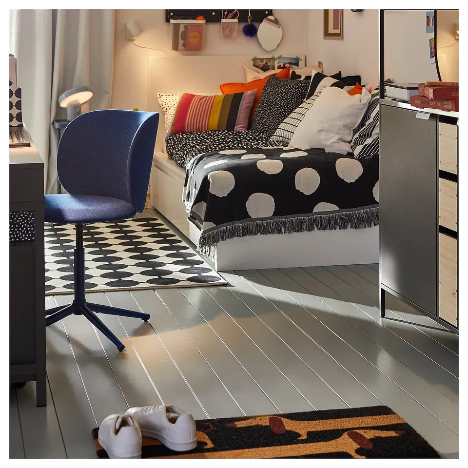 Modern bedroom with black, white, and colourful patterned textiles. Blue chair, polka dot rug, and black and white bedding.