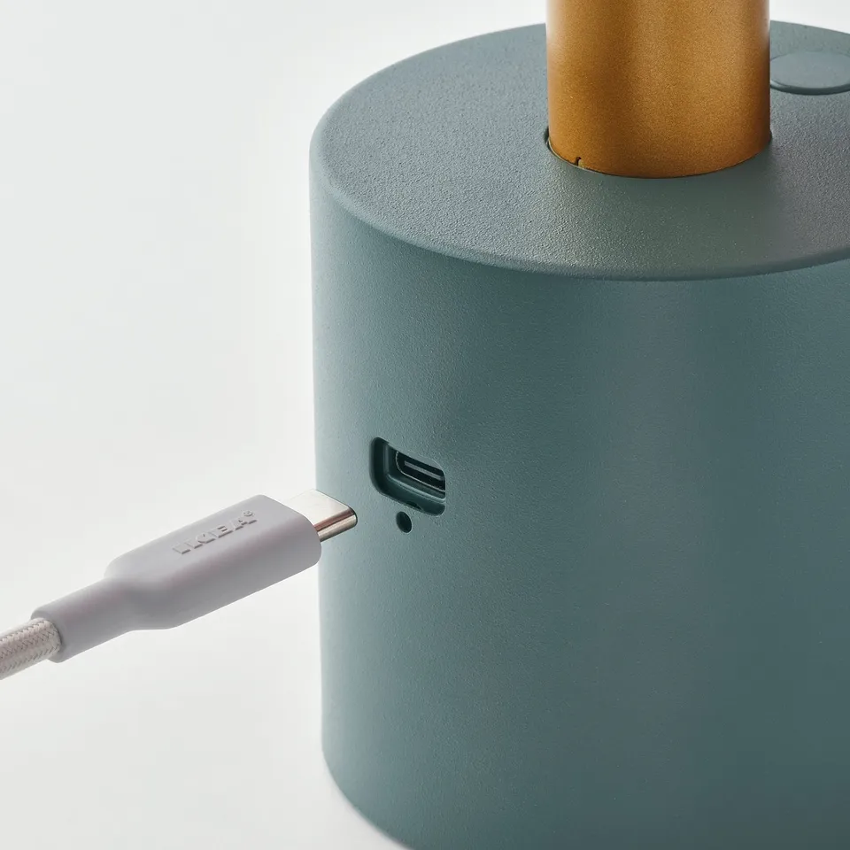 A green portable lamp with a gold top. It charges via usb-c, giving soft, warm light.
