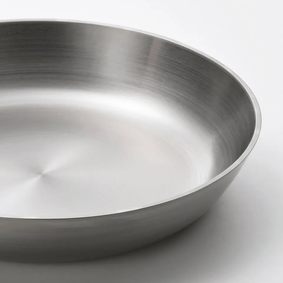Polished stainless steel frying pan shown from above, highlighting smooth, reflective surface and sleek, sloping handle.