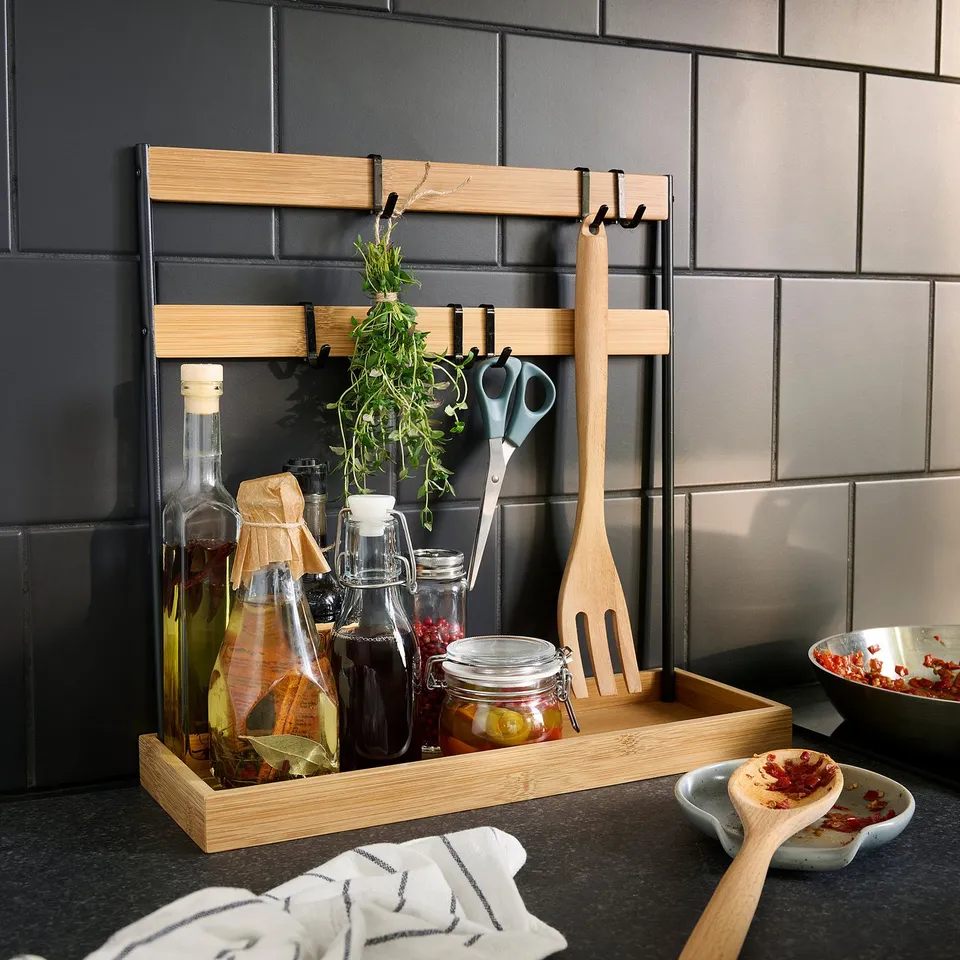 Wooden kitchen organiser with hooks holds utensils, bottles, and herbs on counter.