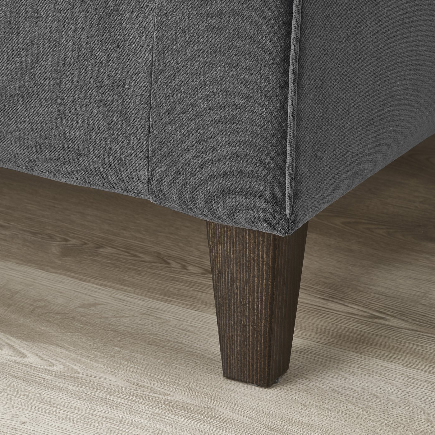 Are grey sofa corner, wood floor visible. Soft cover, sturdy dark leg shown, comfy & durable.