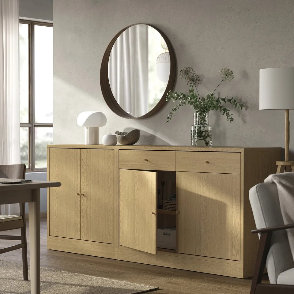 Modern living room with wooden TONSTAD sideboard, light oak, large round mirror, grey chair, lamp, and plant.