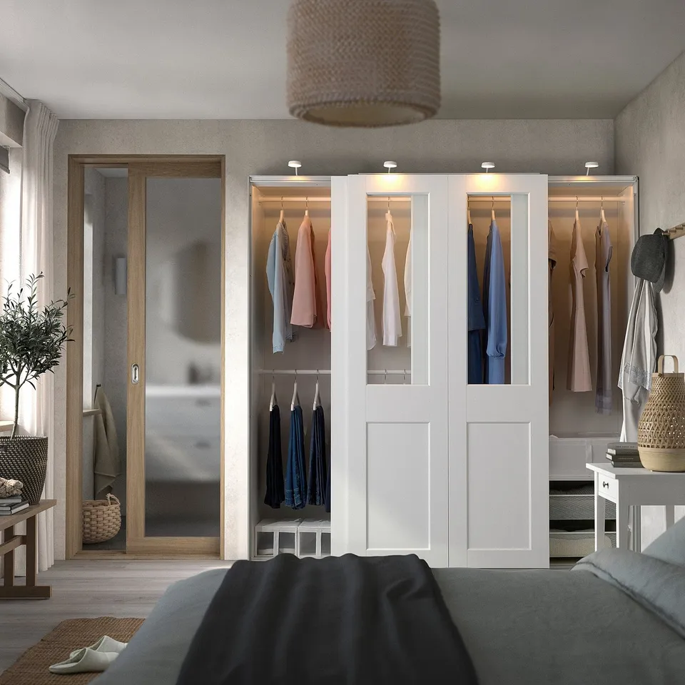 Modern bedroom with large PAX wardrobe, glass panels, and built-in lights. Tall, stylish, with cosy pendant lamp, bed, bench, and plant.