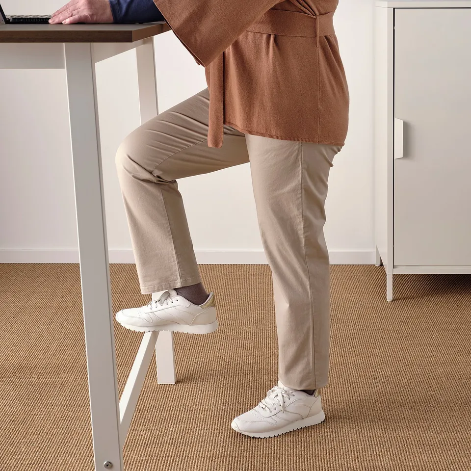 Person leaning on high table with feet on footrest, showcasing MITTZONs sit/stand support feature.