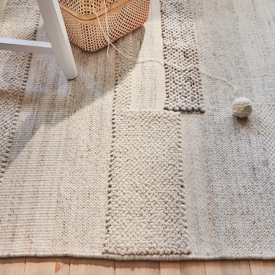 Handwoven, textured beige rug, cotton backing, wooden floor, wicker basket.