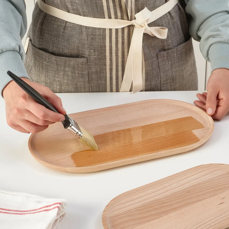 A person oils a wooden serving tray, enhancing its finish.