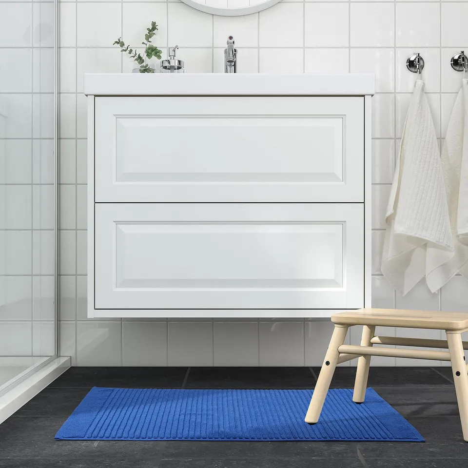 Modern bathroom with blue bath mat contrasting dark floor.