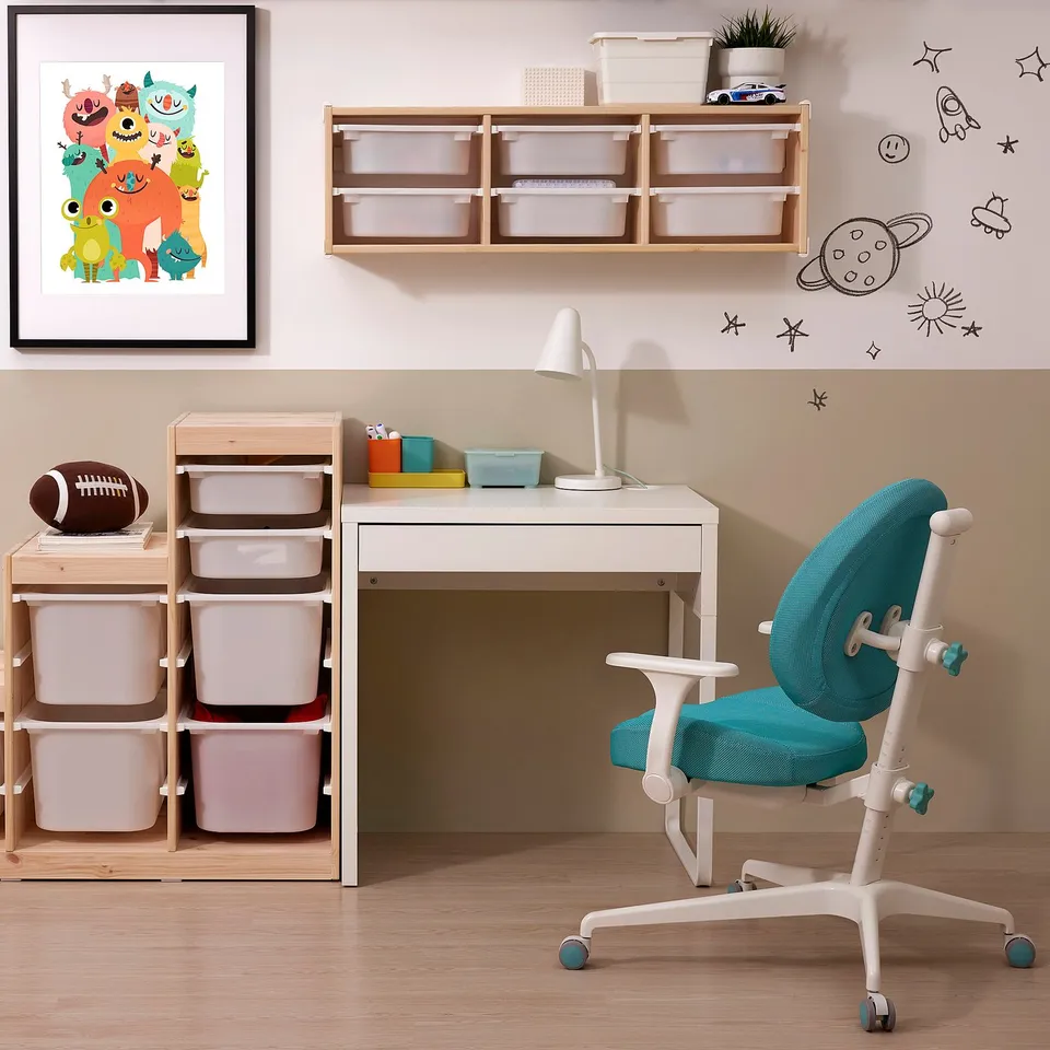 A childs study area: a white desk with drawers and storage bins, a teal desk chair, and a wall shelf with a plant and bins. Bright & neatly arranged.