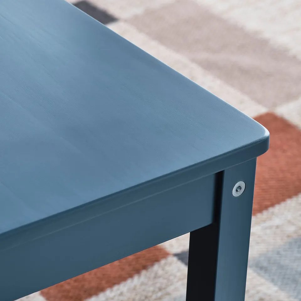 Notched blue wooden table, sleek design highlights smooth finish, placed on multicoloured rug.
