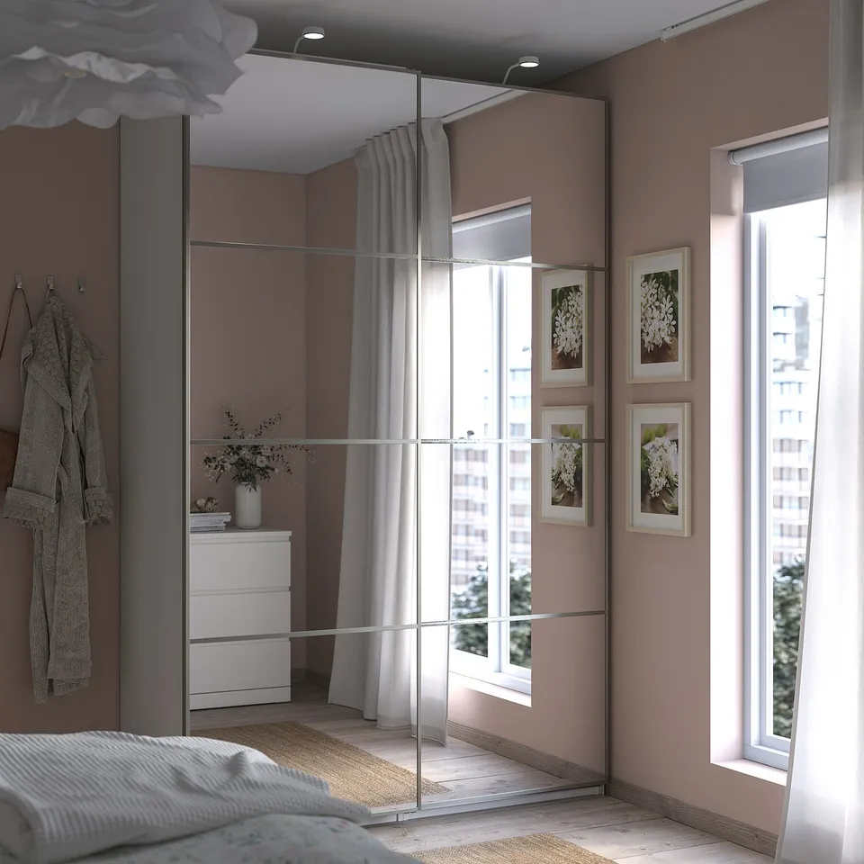 Modern bedroom with mirrored PAX wardrobe, pink walls, white furniture, large window, and floral pictures.