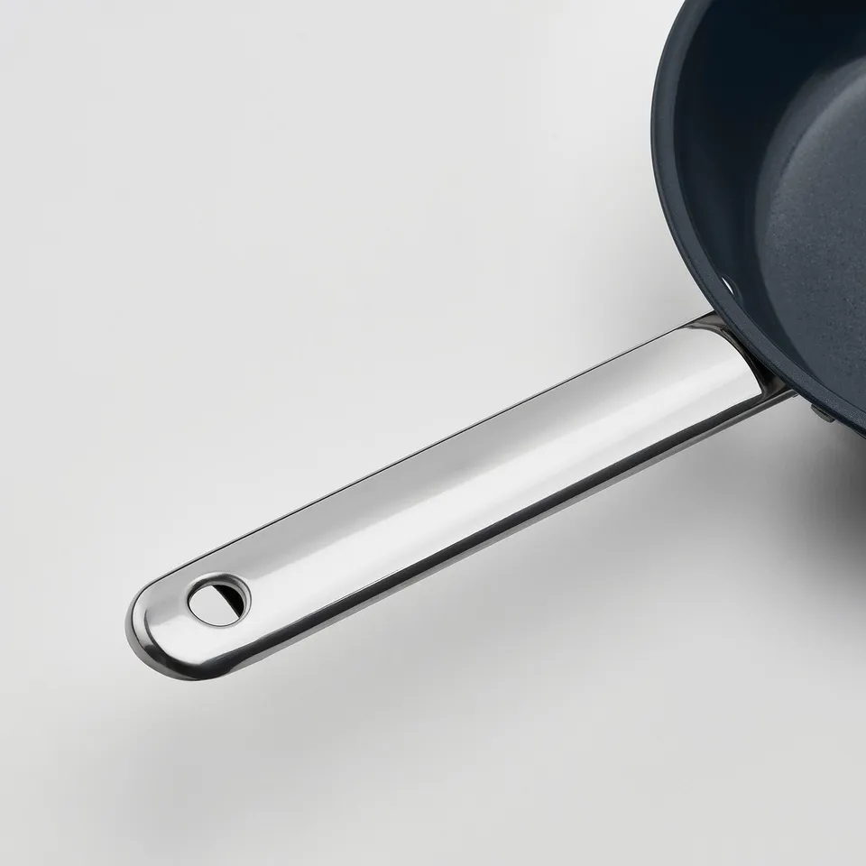 Modern black pan with shiny, ergonomic stainless steel handle. High-quality design for easy cooking and cleaning.