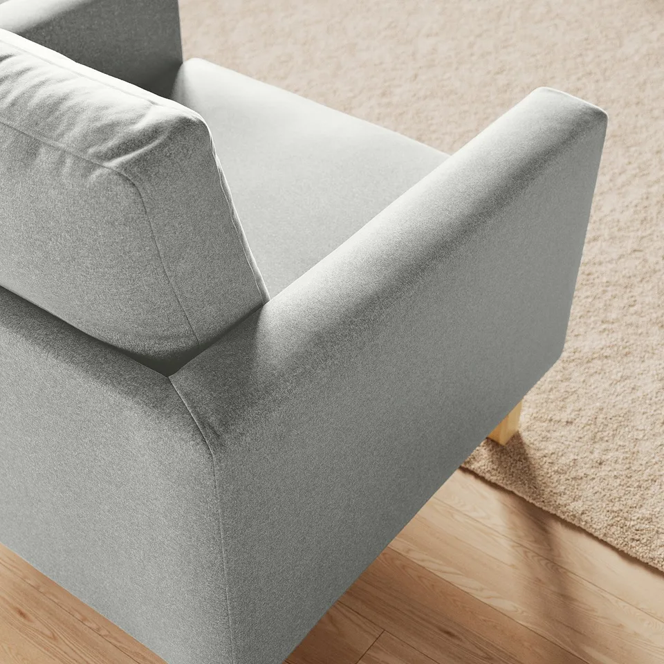 Modern grey armchair with clean lines, soft cushions, and wooden legs on stylish rug.