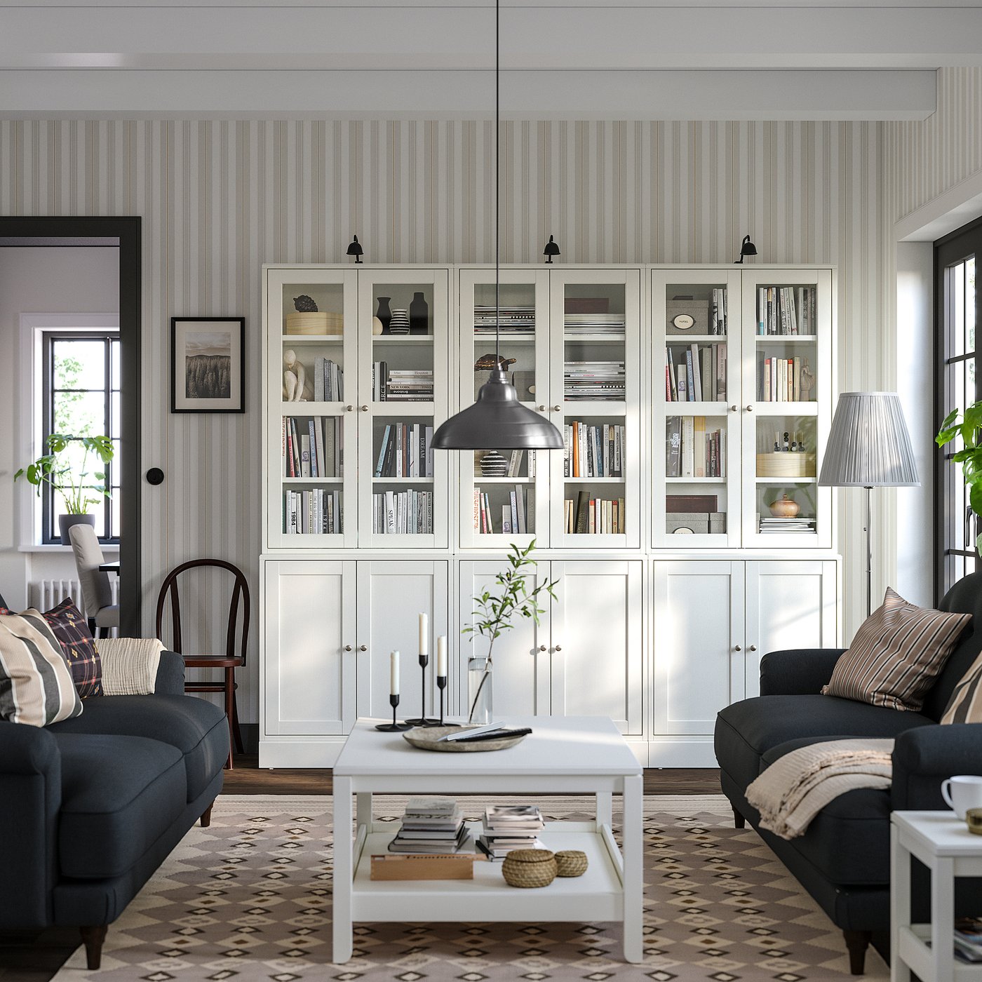 Modern living room with HAVSTA shelves, books, dark couches, white table, patterned rug, striped walls.