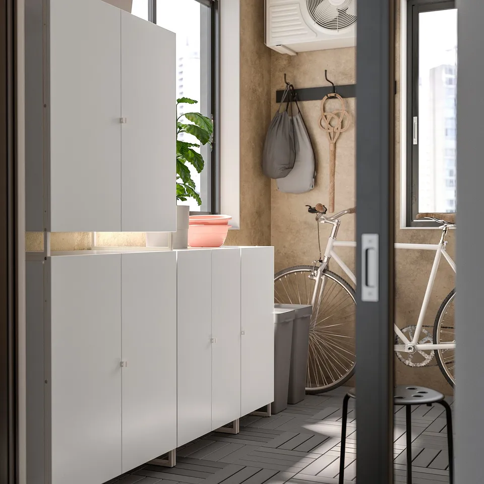 Modern balcony storage unit with white cabinets, grey floor, and potted plant.