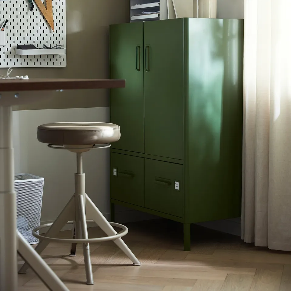 A modern home office an olive green IDÅSEN cabinet with adjustable shelves and a beige swivel stool beside it.