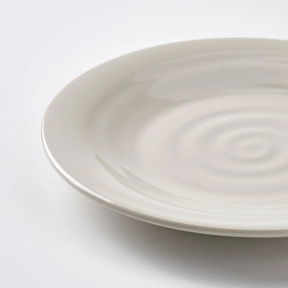 Close-up of an off-white plate with a subtle, rustic texture and gentle waves, set against a plain white background.