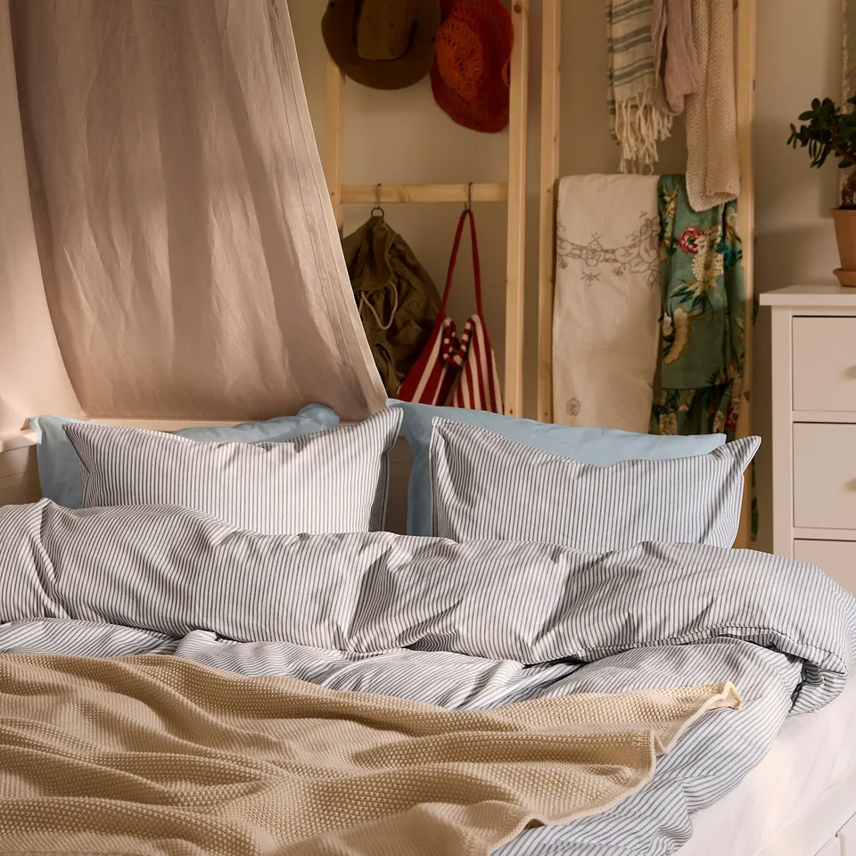 A SOLFIBBLA duvet set in blue and white stripes on a bed, with a canopy and assorted decor.