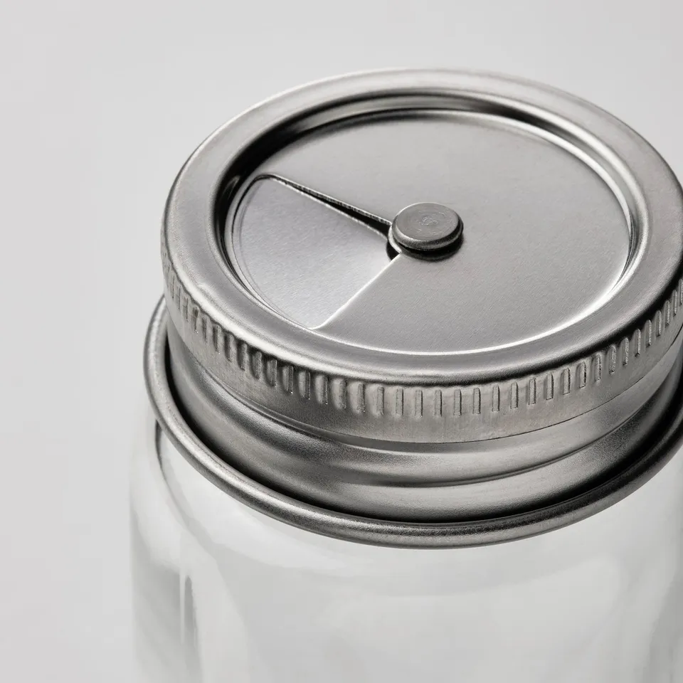 Clear glass jar with stainless steel lid, featuring a lever and textured grip edge for secure sealing.