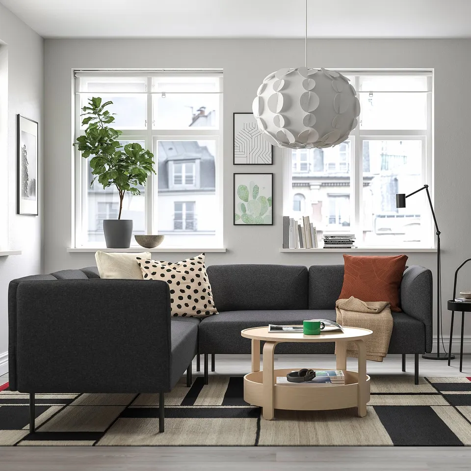 Modern living room with grey LILLEHEM sofa, black-and-white pillows, coffee table, green mug, plant, and pendant light.