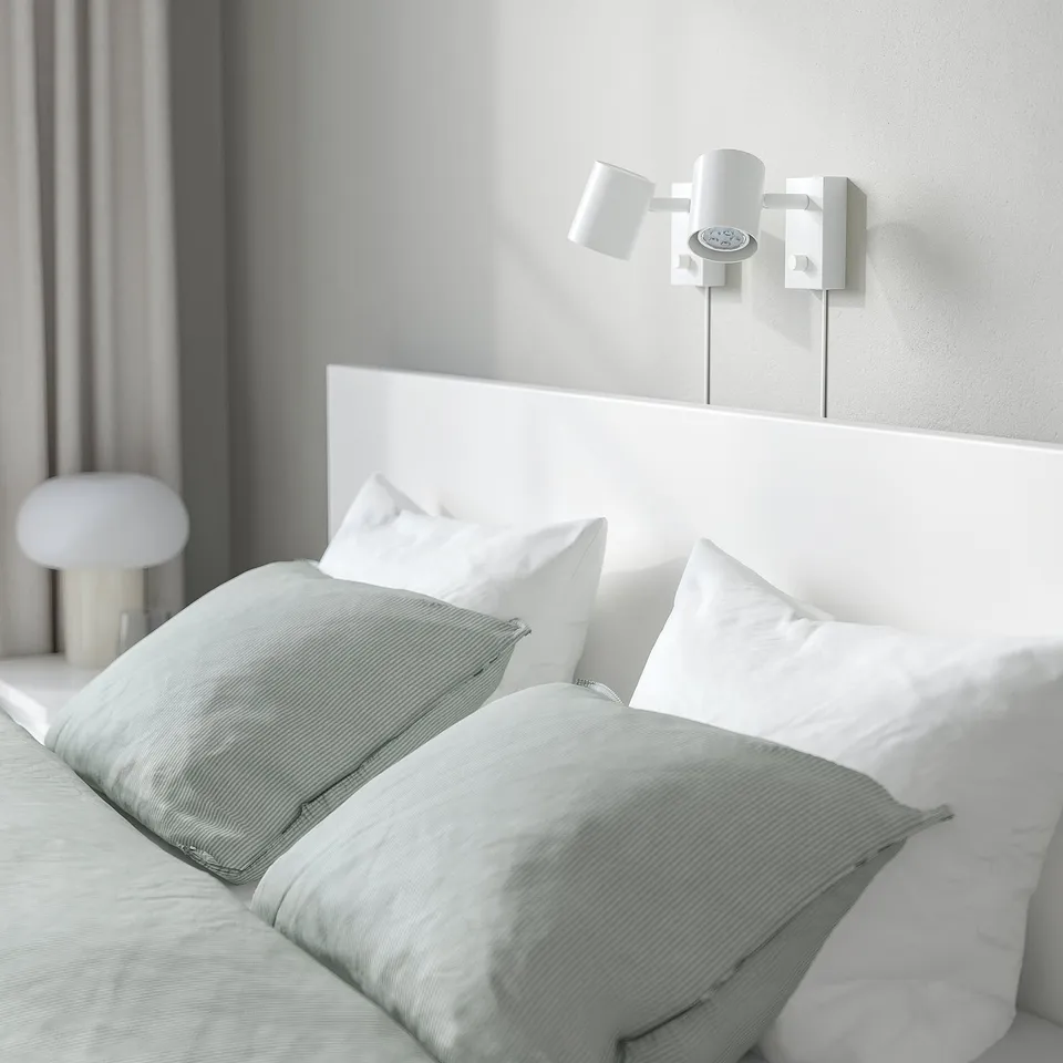 Modern bed with minimalist, white headboard and adjustable bedside lights.