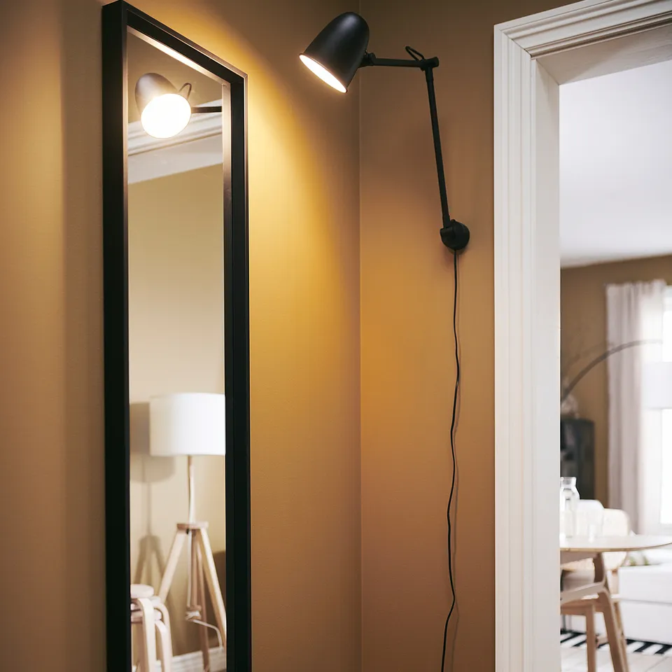 A hallway with a black-framed NISSEDAL mirror, wall lamp, and wire basket holding keys and mail.