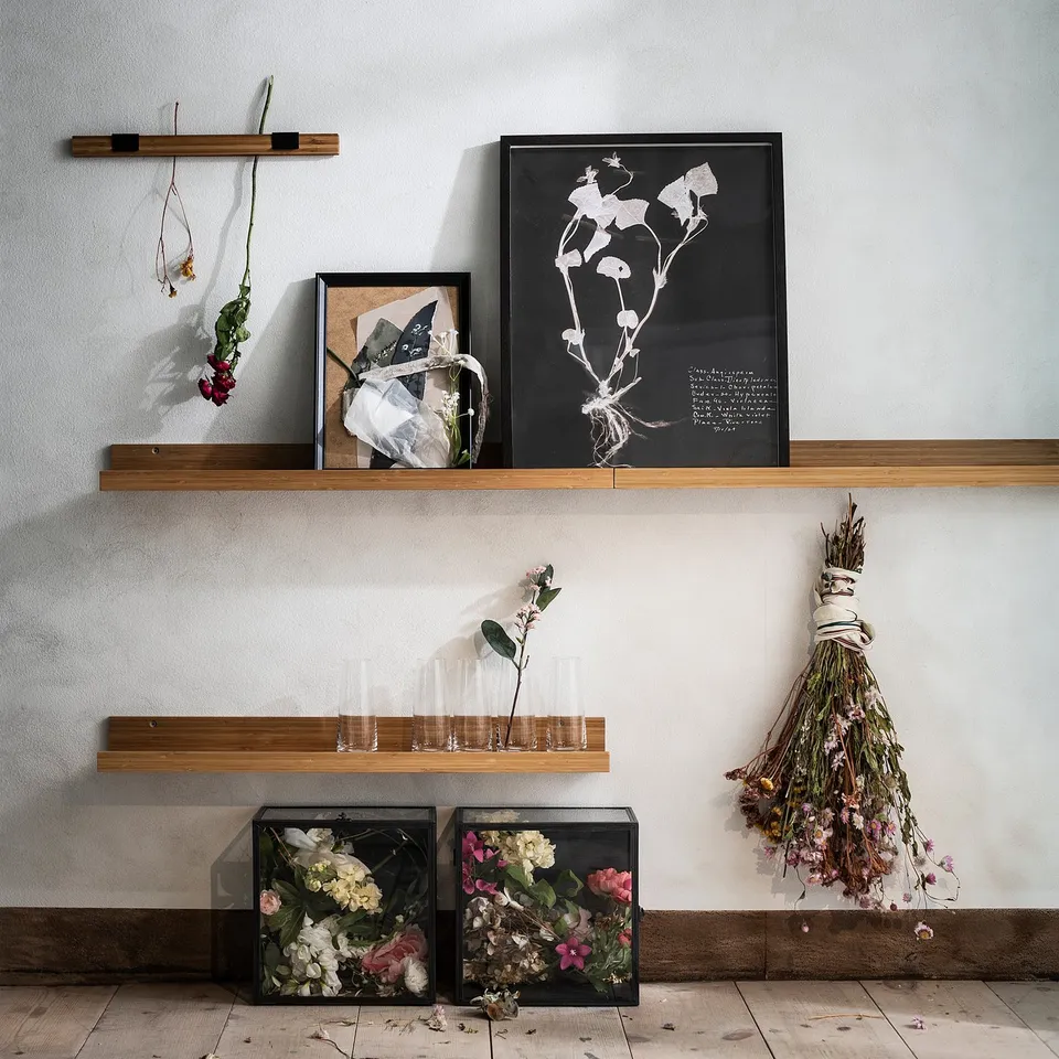 Wooden shelves display flowers, frames, art. Home decor setup with natural elements.